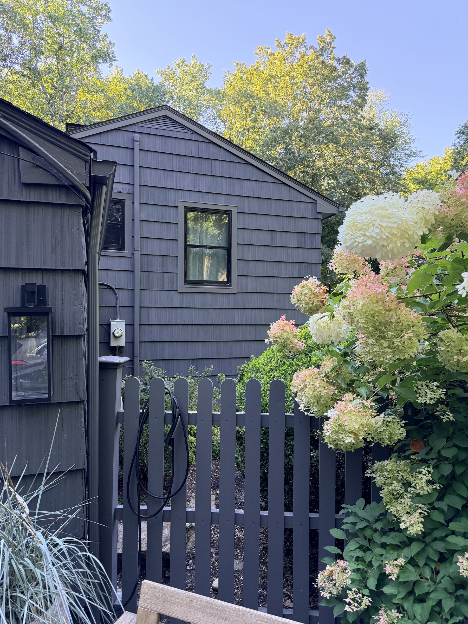 Charcoal shingle siding beside a dark fence and white hydrangeas