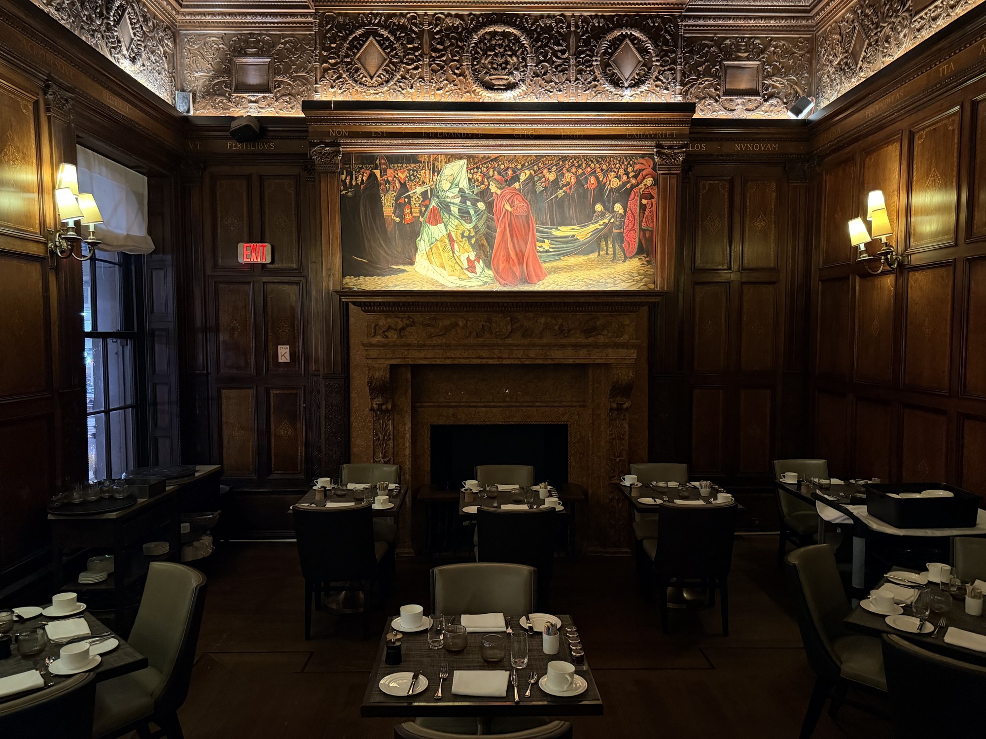 Wood-panelled dining room at the Lotte New York Palace with a carved ceiling, a large painting over the fireplace and tables set with cups