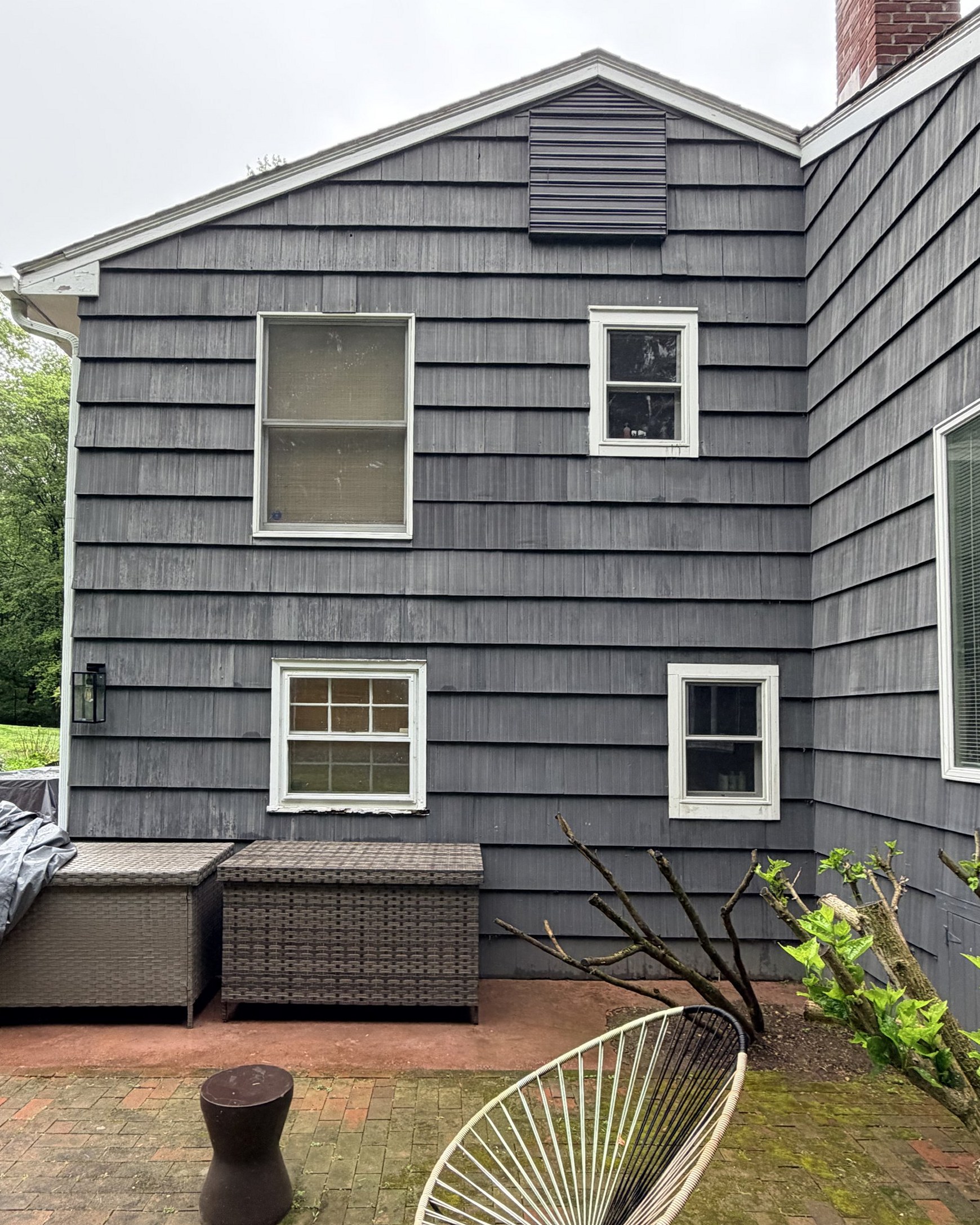 The house before the exterior work: weathered, streaked grey shingle siding and deteriorating white wooden window frames above a brick patio